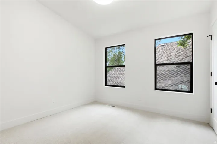 Bright room featuring two large windows with black frames, white walls, white trim, light-colored carpeting, and a flush-mount ceiling light