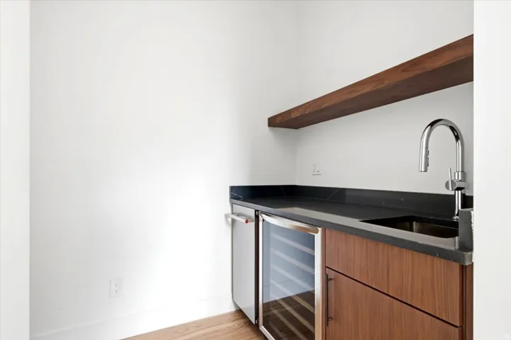 Wet bar featuring a dark stone countertop, wood-finish cabinetry, under-counter beverage cooler, and a floating wood-finish shelf