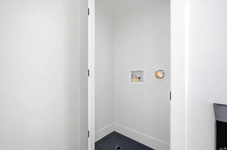 Dedicated laundry area featuring a wall-mounted utility box, dark tile flooring, and white baseboards