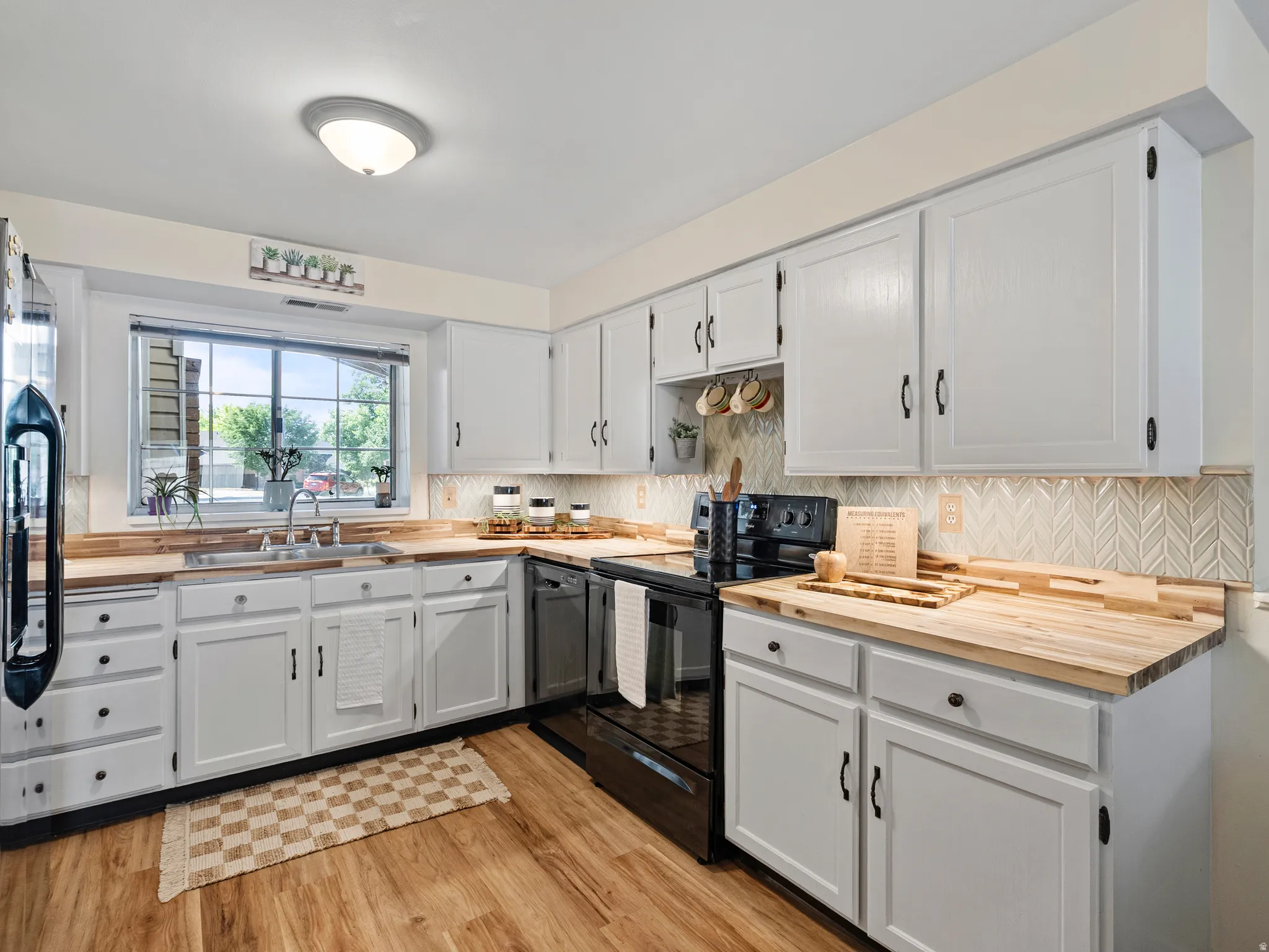 Contemporary kitchen featuring white cabinetry, butcher block countertops, and a decorative herringbone tile backsplash with lovely under cabinet lighting