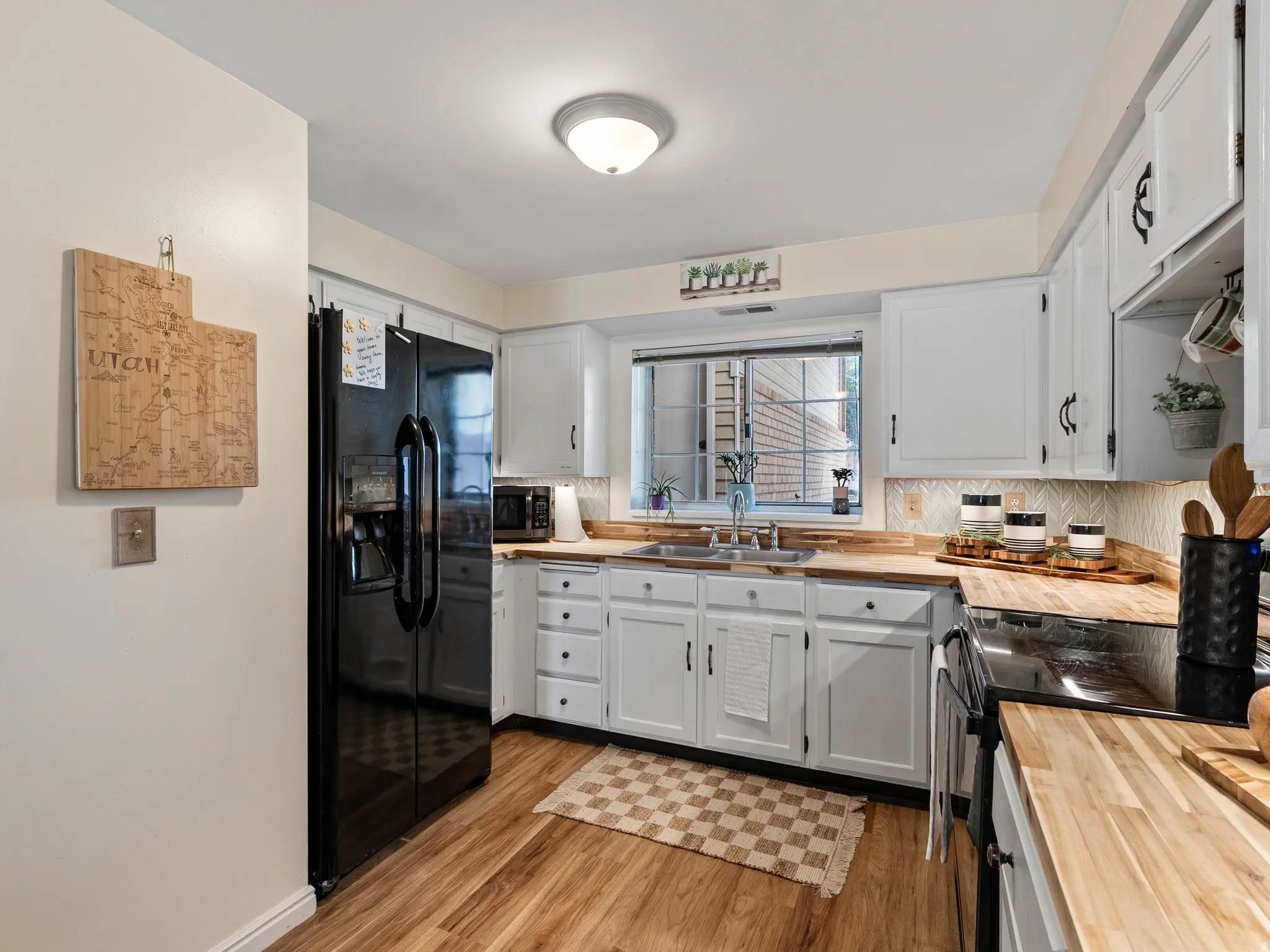 Kitchen featuring new lvp flooring, white cabinetry with dark hardware, butcher block countertops, and a full suite of black appliances
