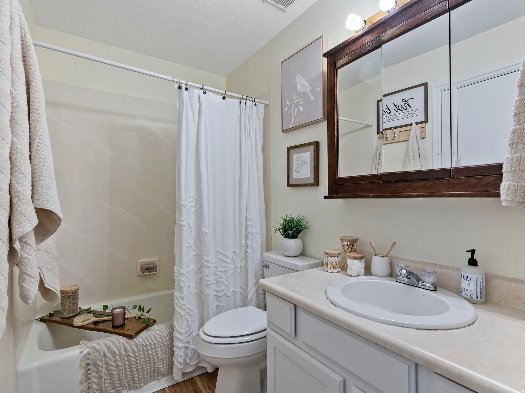 Bathroom featuring a built-in bathtub with shower, a toilet, a vanity with an integrated sink, and a framed medicine cabinet with overhead lighting