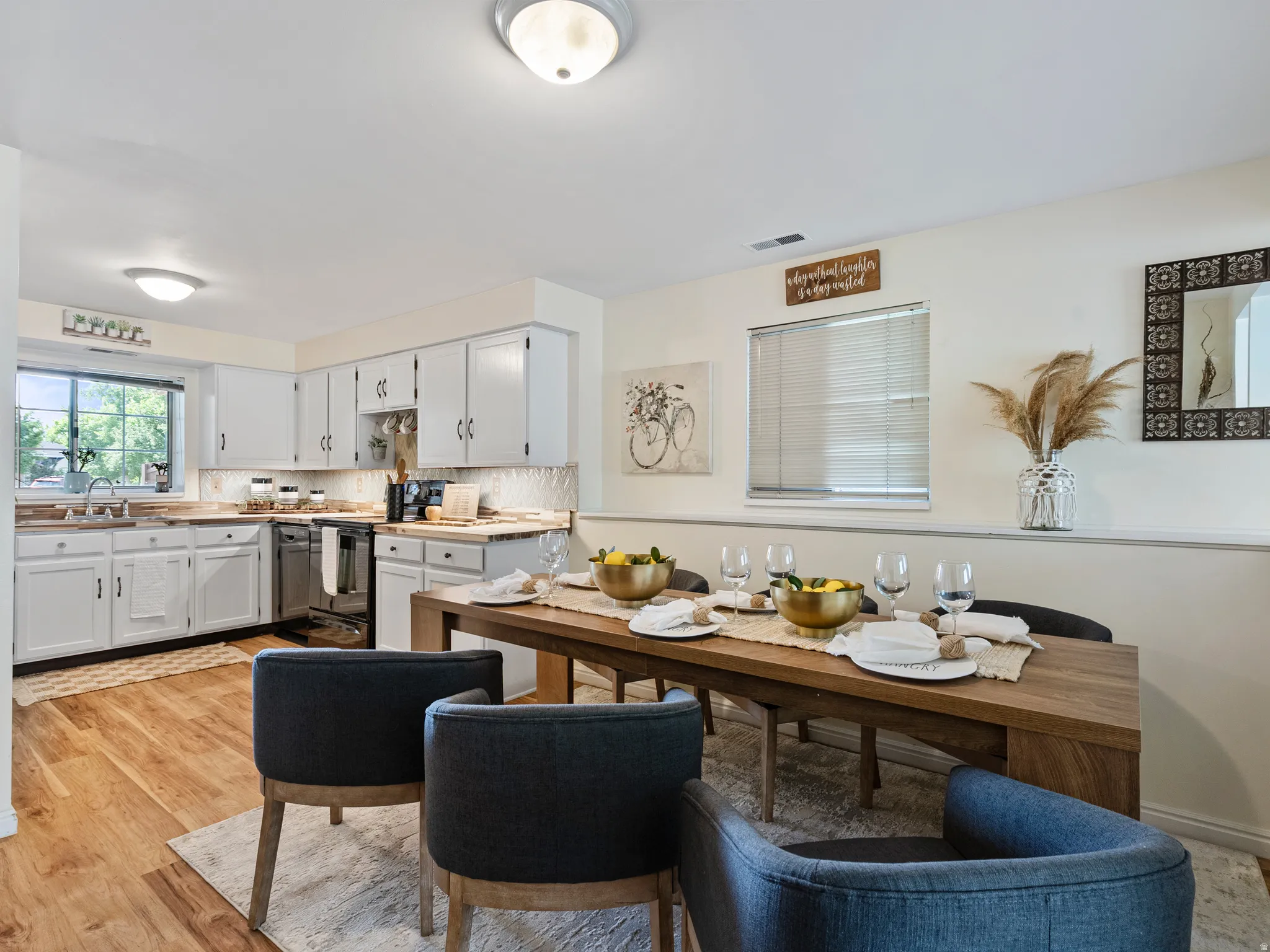 Open-concept kitchen and dining area featuring wood-finish flooring, white cabinetry, stainless steel appliances, a tile backsplash, and a dining space with a natural wood-finish table