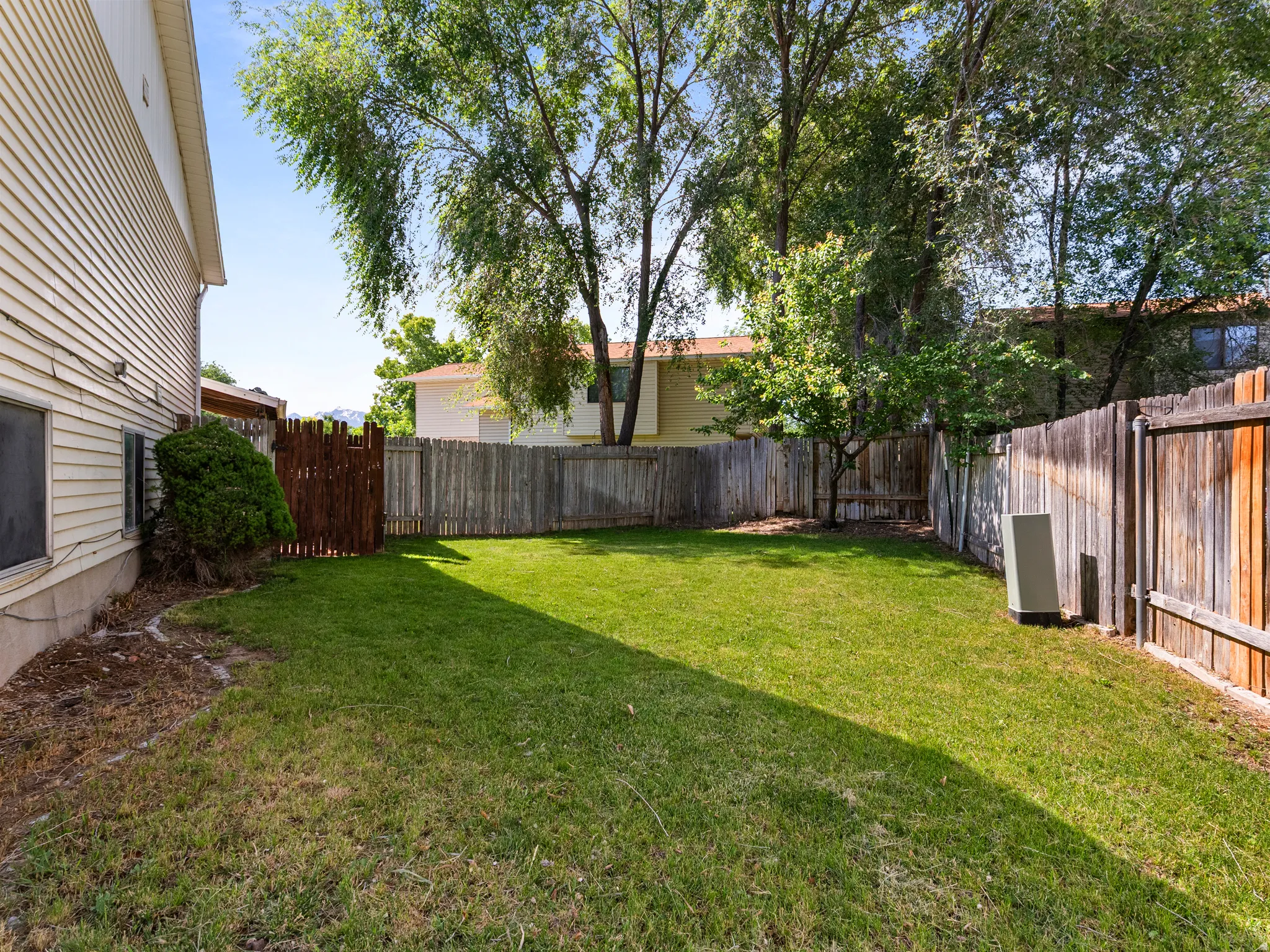 Expansive lawn area featuring a wood privacy fence, mature trees, and a wooden gate