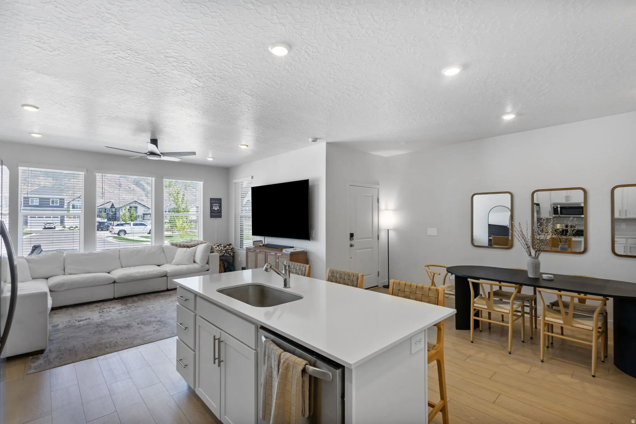 Open-concept living area with a kitchen island featuring a stainless steel sink, light-toned cabinetry, and a white countertop