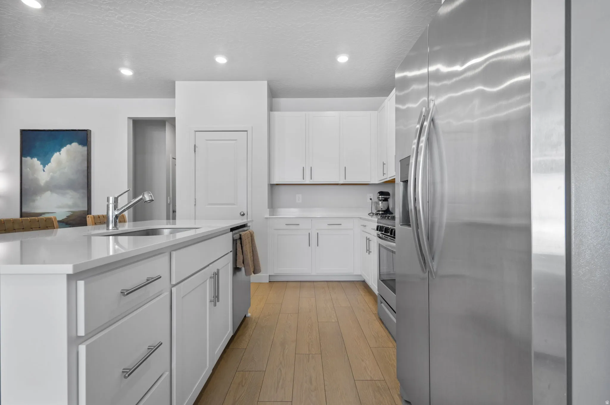 Modern kitchen featuring white cabinetry with silver hardware, light wood-finish flooring, and a large central island with an undermount sink