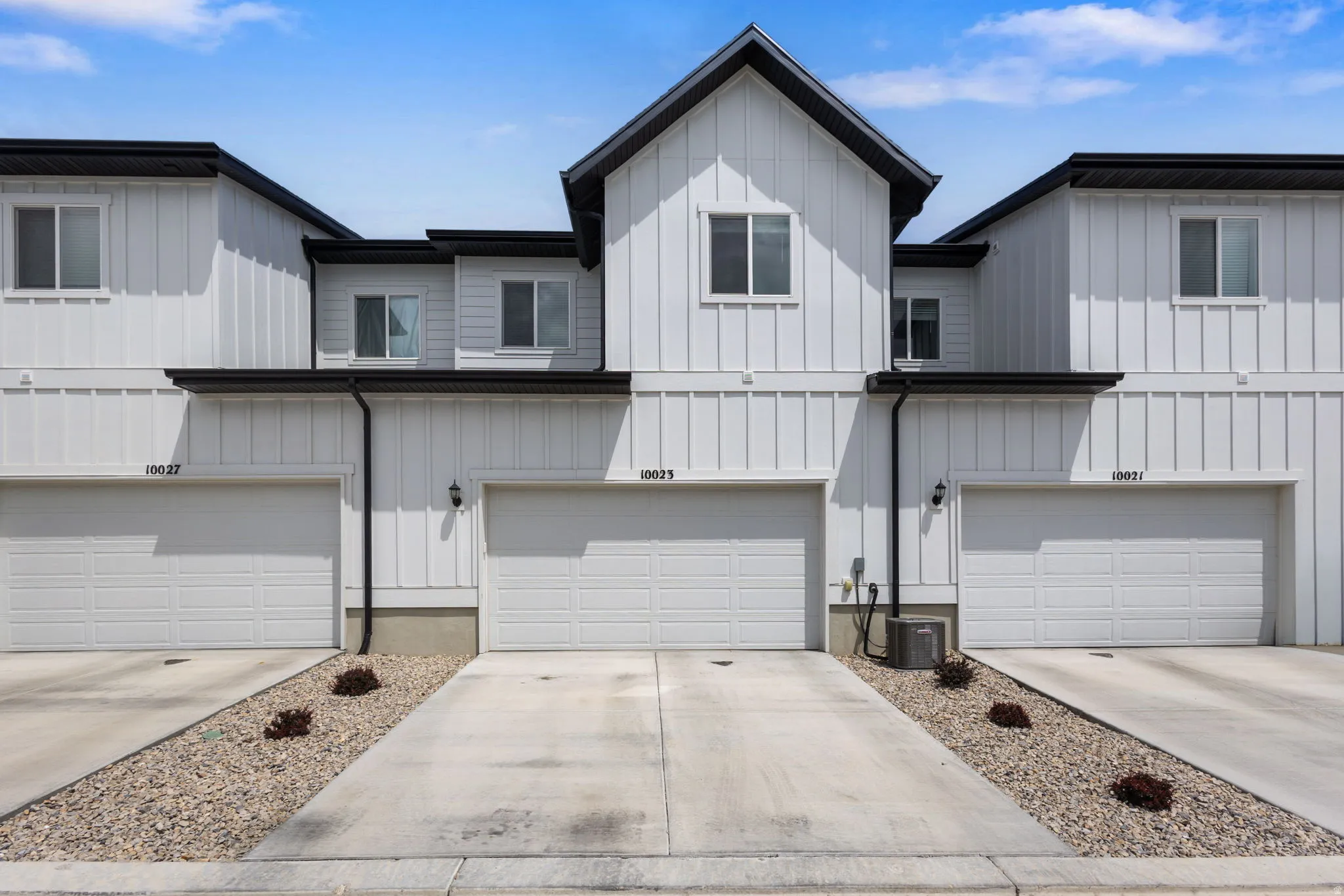 Modern townhome exterior featuring white board and batten siding, black trim, and a prominent gable roofline