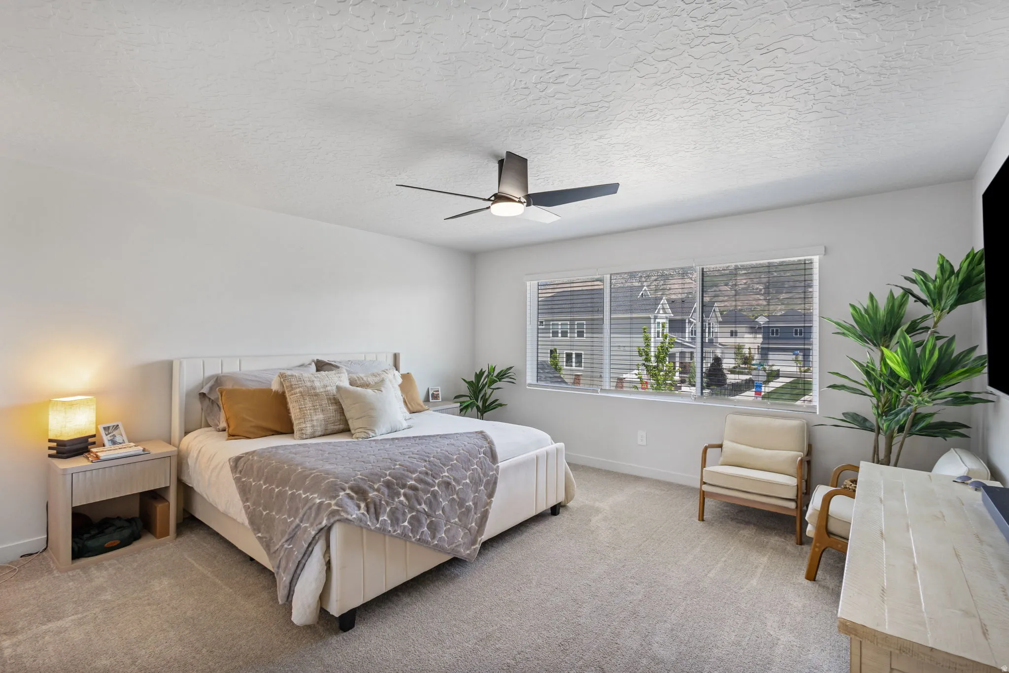 Spacious room featuring light gray carpeting, neutral wall colors, a large window with blinds, and a ceiling fan with integrated lighting