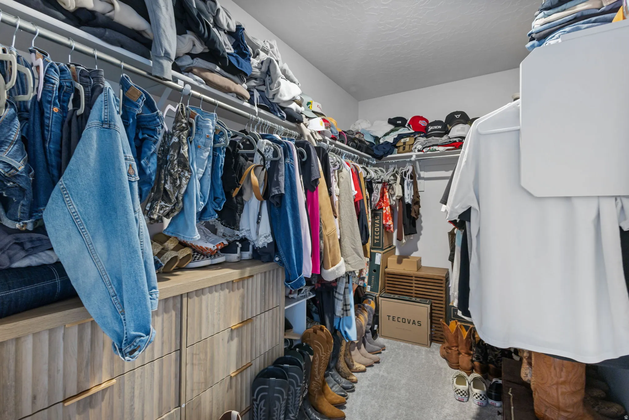 Walk-in closet featuring built-in wood-finish drawers with modern hardware, extensive clothing rods, and overhead shelving