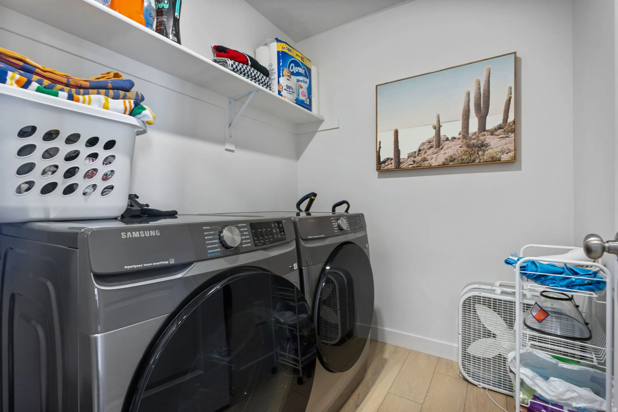 Dedicated laundry area featuring a full-size front-load washer and dryer set, white wall shelves for storage, light wood-finish flooring, and light-toned wall paint