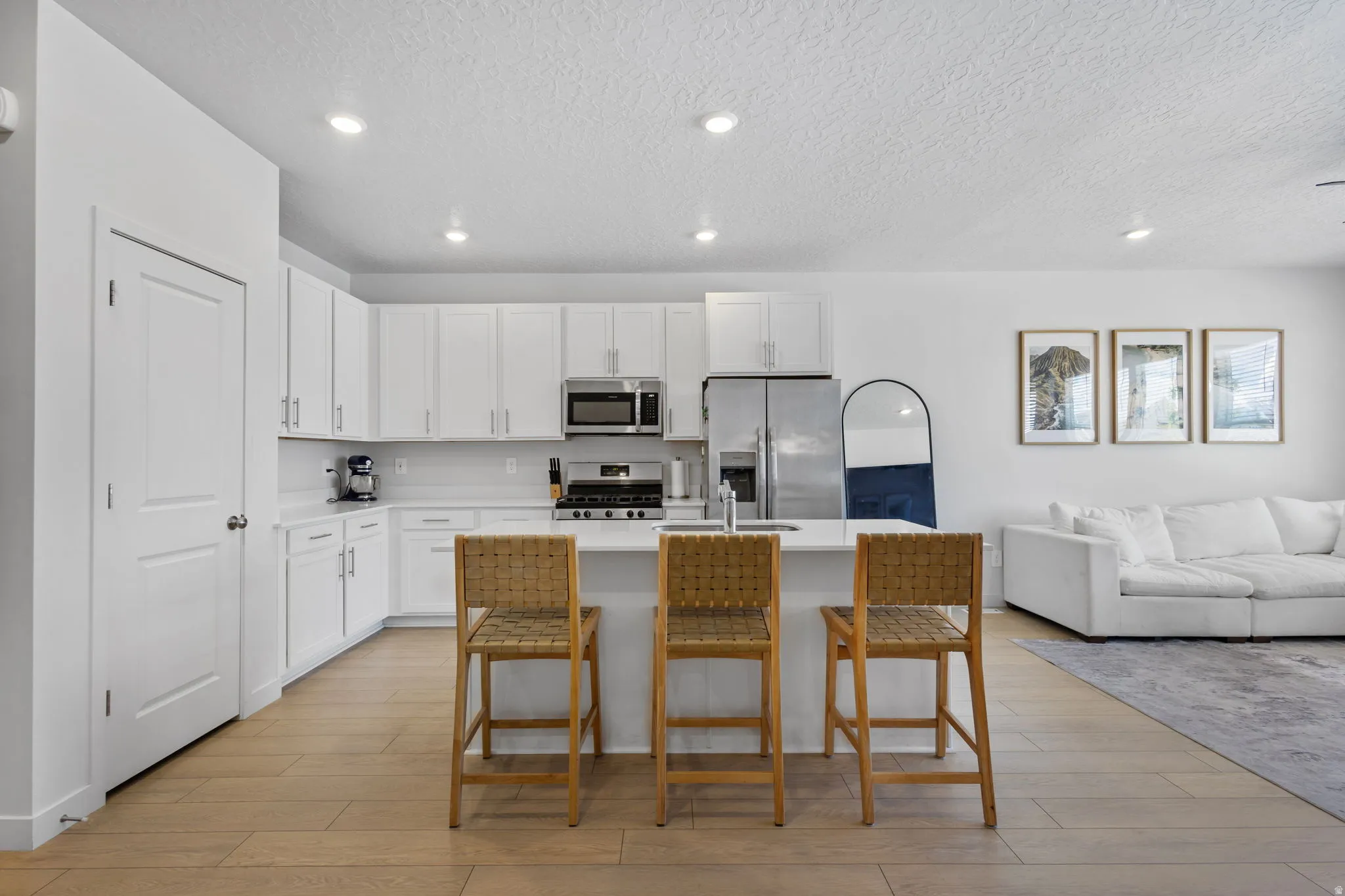 Modern kitchen featuring white cabinetry, stainless steel appliances, a center island with bar seating, recessed lighting, and wood-finish flooring