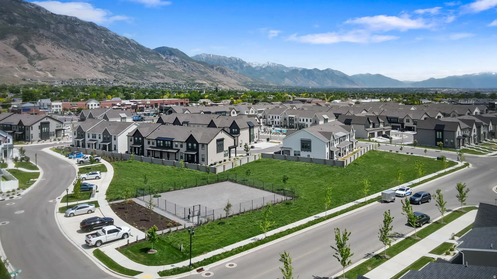 Modern residential development featuring townhomes with dark gray and white exteriors, asphalt shingle roofs, and paved streets