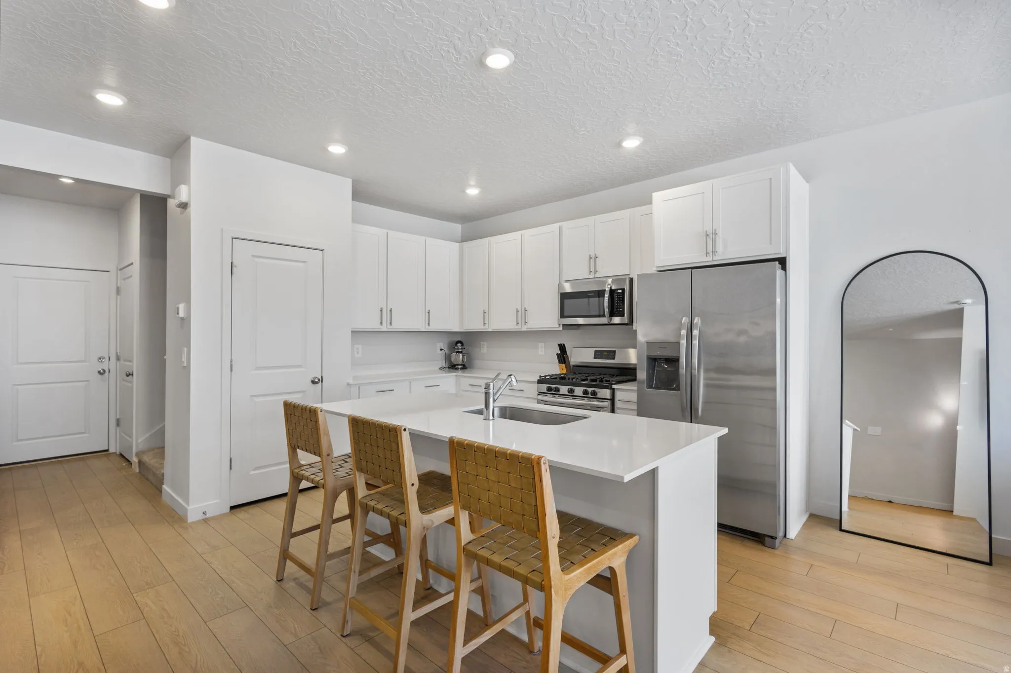 Bright kitchen featuring white cabinetry, a large center island with seating, stainless steel appliances, and light wood-finish flooring