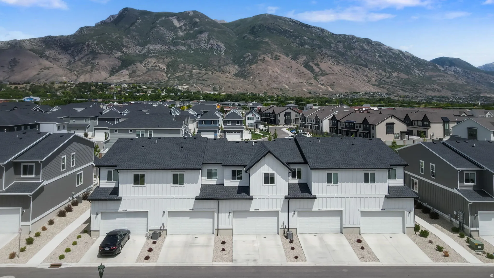 Modern townhome architecture featuring white vertical siding, dark shingle roofing, and attached garages