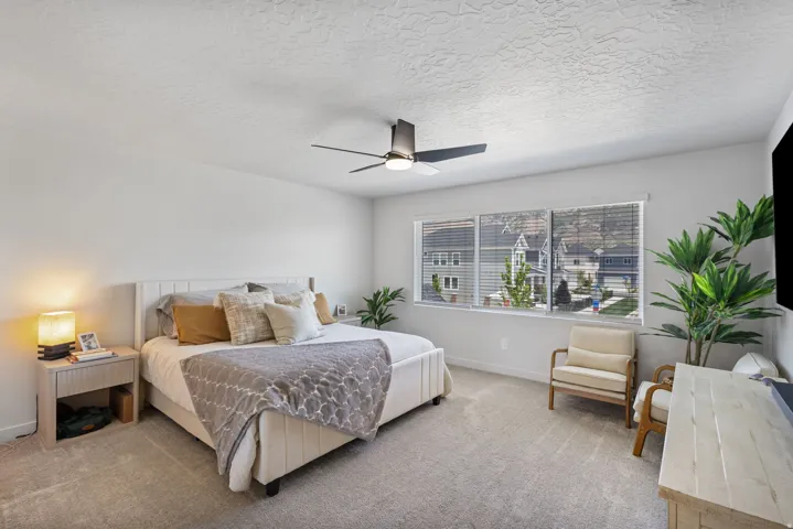 Spacious room featuring light gray carpeting, neutral wall colors, a large window with blinds, and a ceiling fan with integrated lighting
