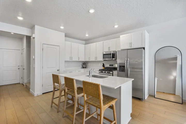 Bright kitchen featuring white cabinetry, a large center island with seating, stainless steel appliances, and light wood-finish flooring