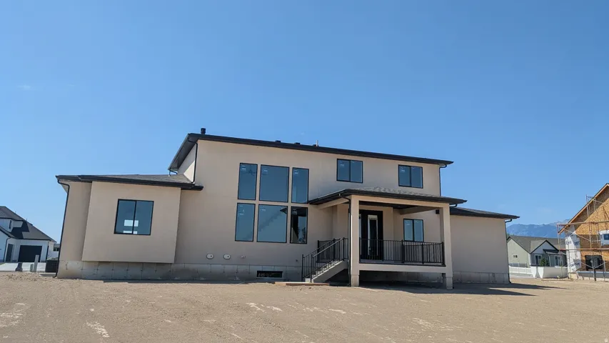 Two-story stucco exterior featuring multiple large windows, a covered patio with black railings, and an exterior staircase