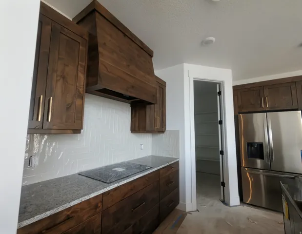 Kitchen featuring rich wood cabinetry, a built-in wood range hood, a herringbone tile backsplash, and stone countertops