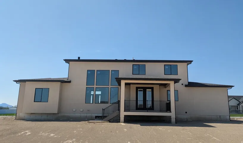 Contemporary stucco exterior featuring a tiered roofline, expansive multi-pane windows, a covered balcony with a black metal railing, and double French doors