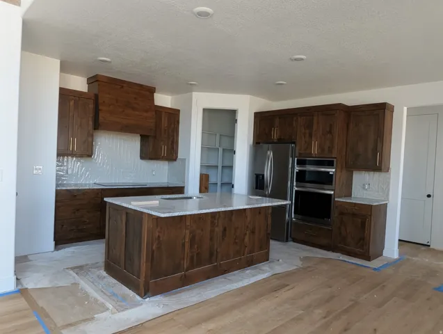 Kitchen featuring dark wood-finish cabinetry, a large center island with a light-toned countertop, stainless steel appliances, and wood-finish flooring