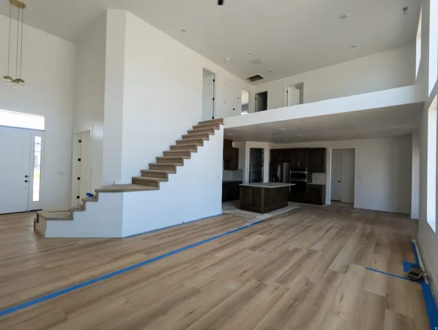 Expansive living area featuring light wood-finish flooring, a two-story ceiling, a carpeted staircase, and an upper-level loft