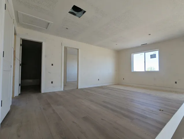 Spacious interior room featuring wood-finish flooring, white walls, and a large window providing ample natural light