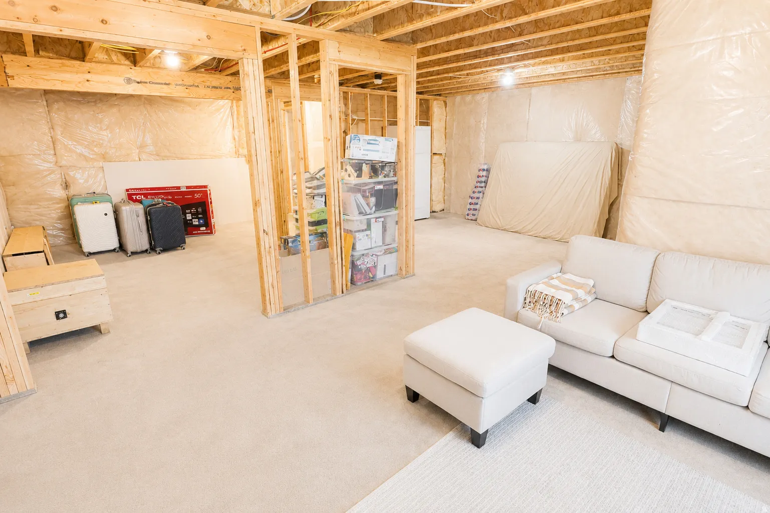 Unfinished basement with exposed wood framing and ceiling joists, featuring carpeted flooring and insulated walls