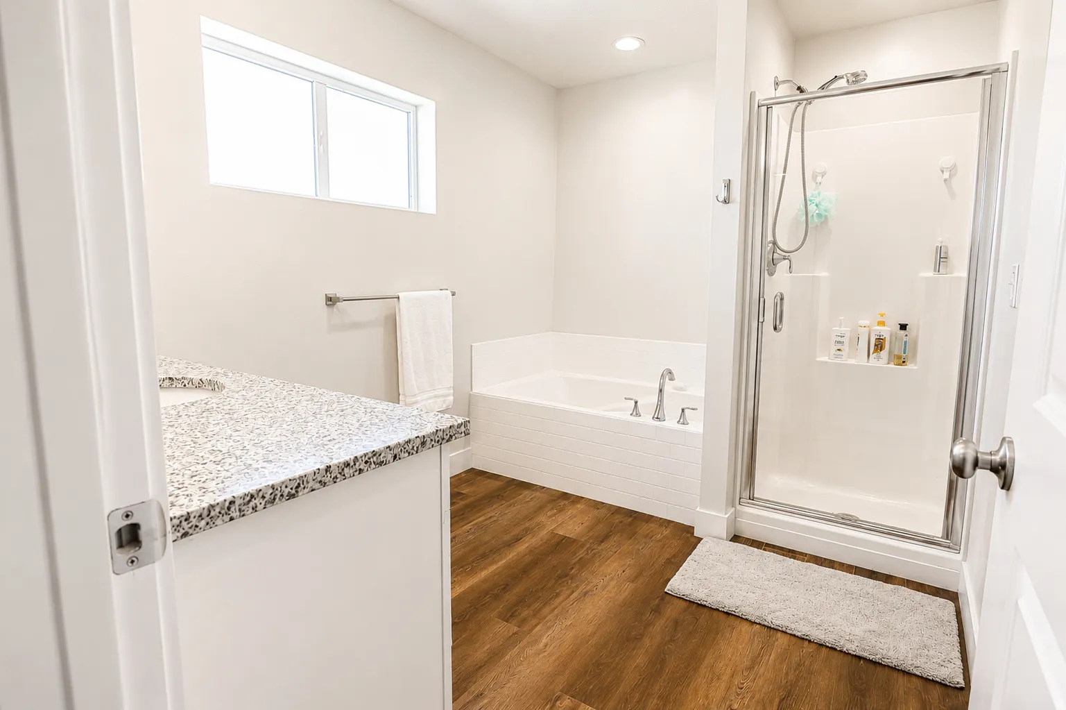 Bathroom featuring a glass-enclosed shower, built-in soaking tub, wood-finish flooring, and a vanity with a speckled countertop