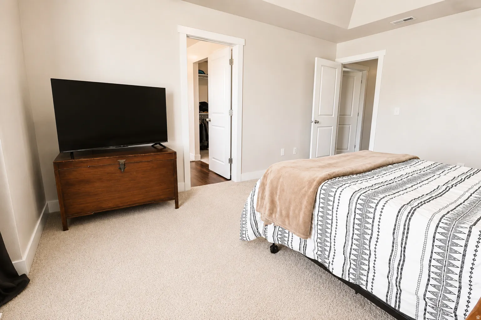 Plush carpeted bedroom featuring neutral wall tones, white trim, and a tray ceiling