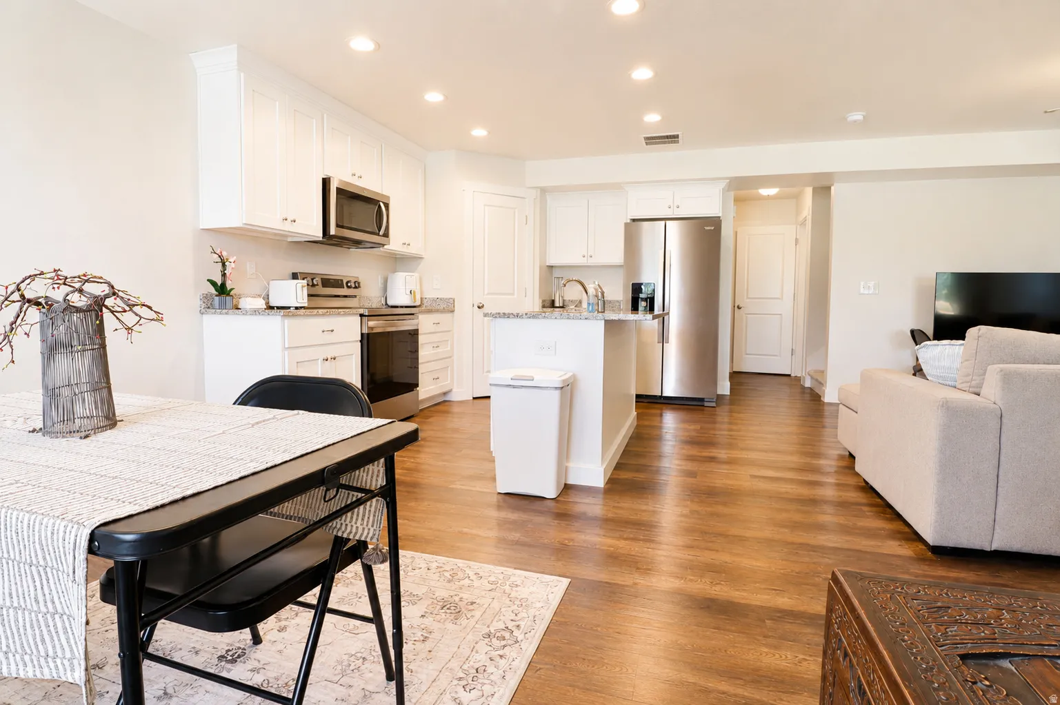 Open-concept kitchen and living area featuring wood-finish flooring, white cabinetry, a kitchen island with sink, stainless steel appliances, and recessed lighting