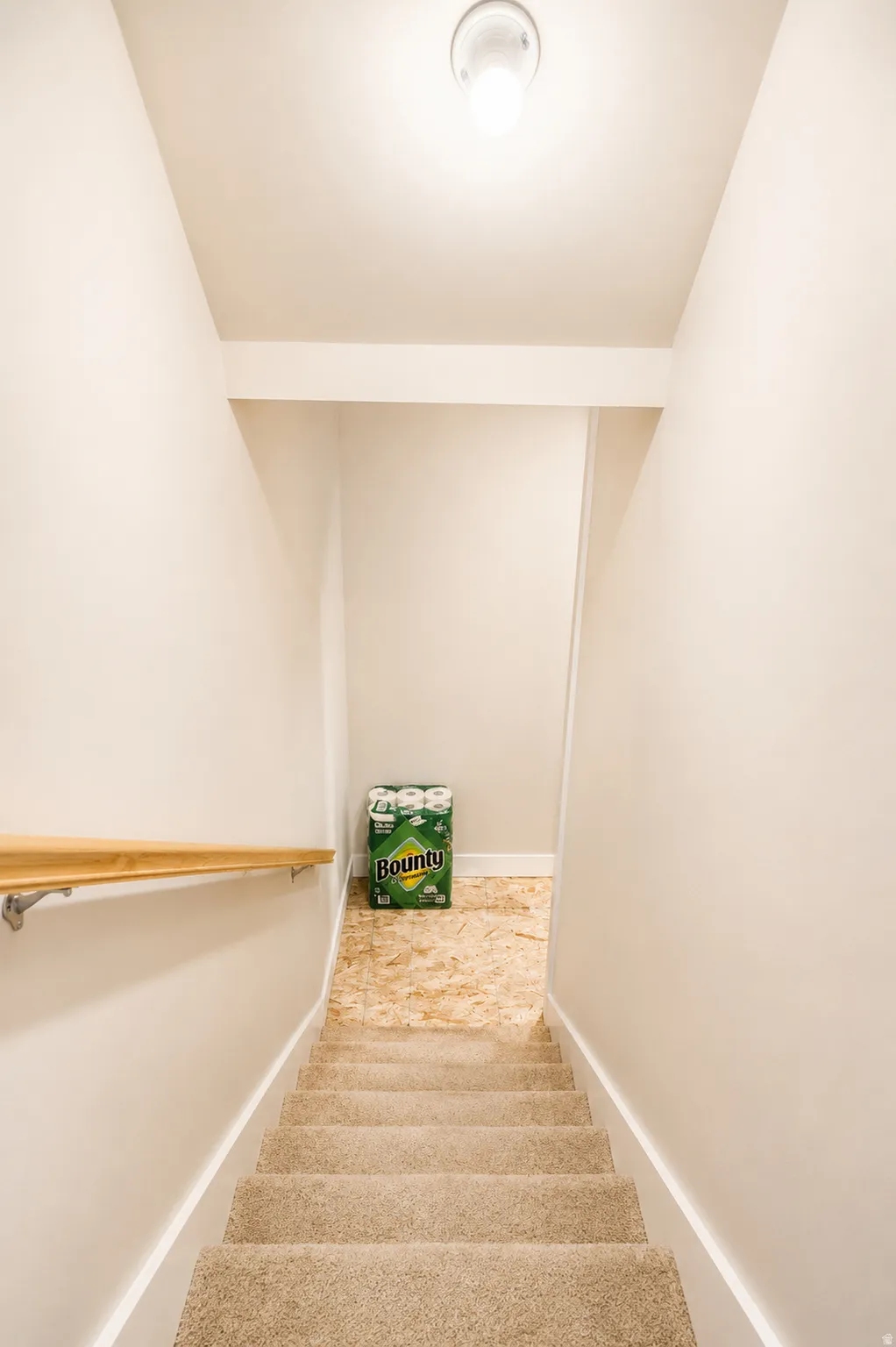 Carpeted staircase with a natural wood handrail, leading to a landing with a light-colored subfloor
