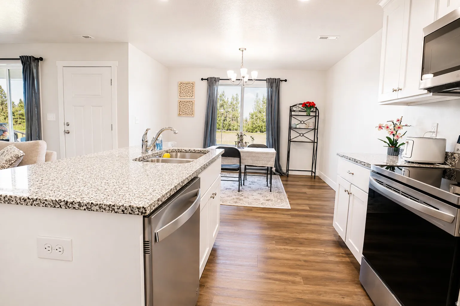 Kitchen featuring an island with a dual-basin stainless steel sink, stainless steel dishwasher, white cabinetry, and light-toned speckled countertops