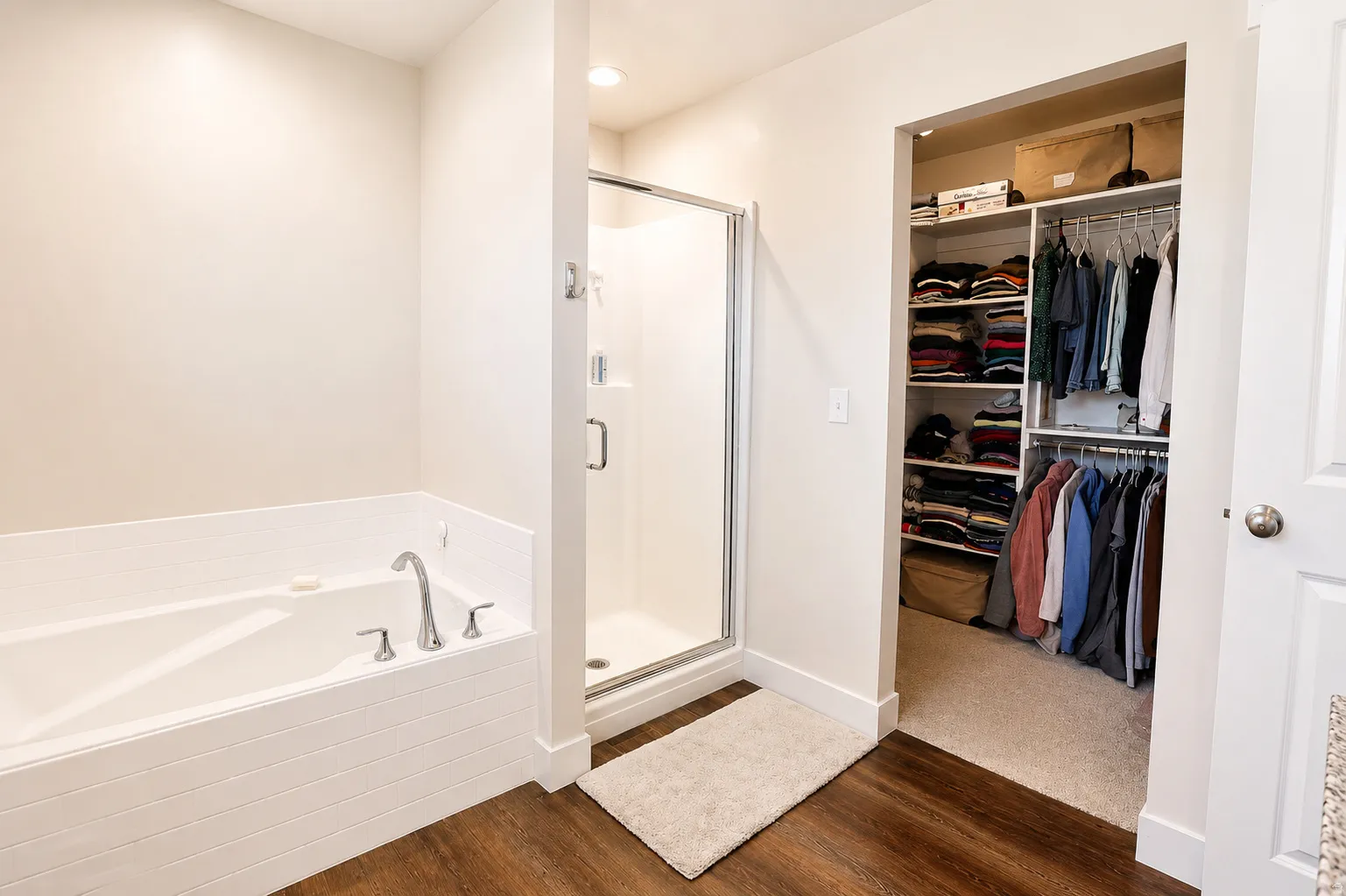 Soaking tub with brushed chrome fixtures, glass-enclosed shower, and wood-finish flooring