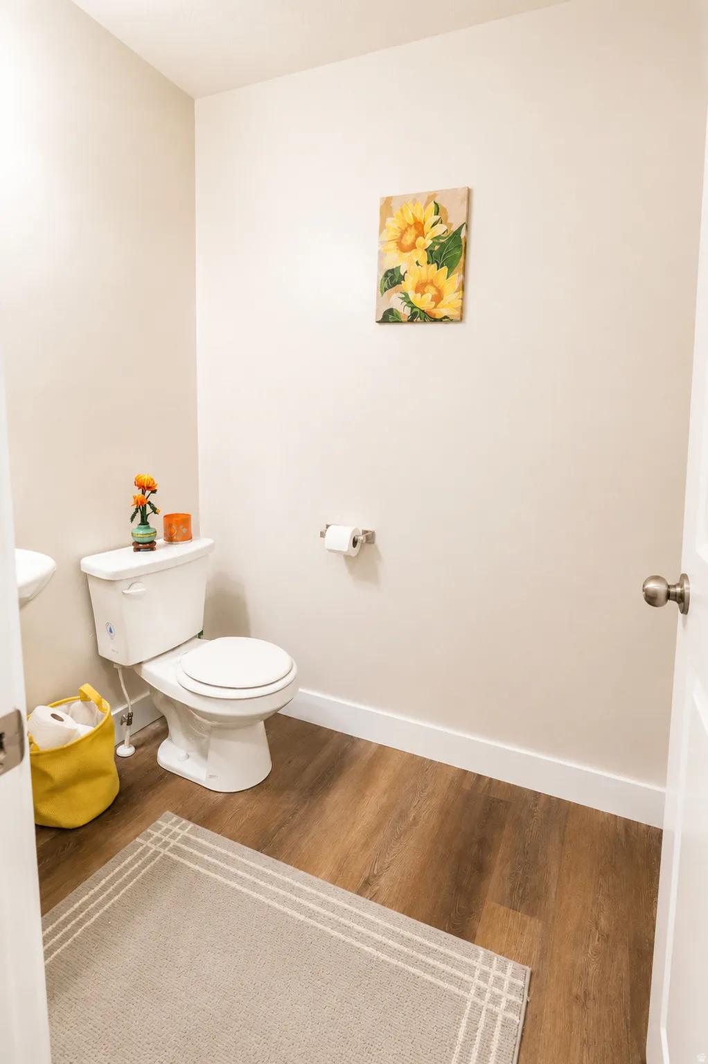 Powder room with wood-finish flooring, white baseboards, and a white toilet