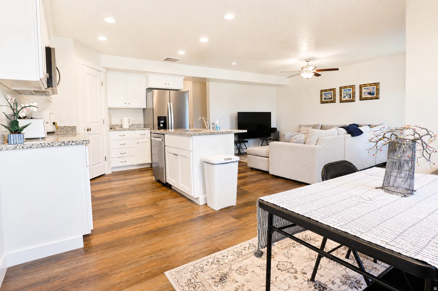 Open-concept living area featuring wood-finish flooring, white cabinetry, and stainless steel appliances
