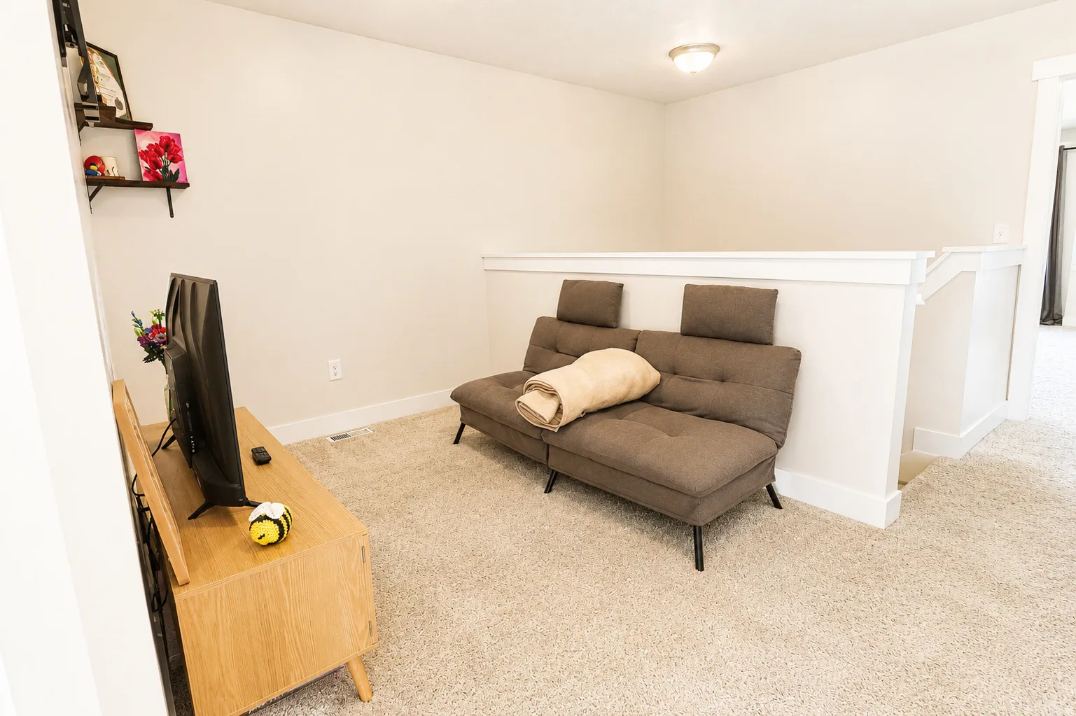 Carpeted upper-level space featuring a contemporary wood-finish media console, neutral wall paint, white trim, and a semi-flush ceiling light fixture