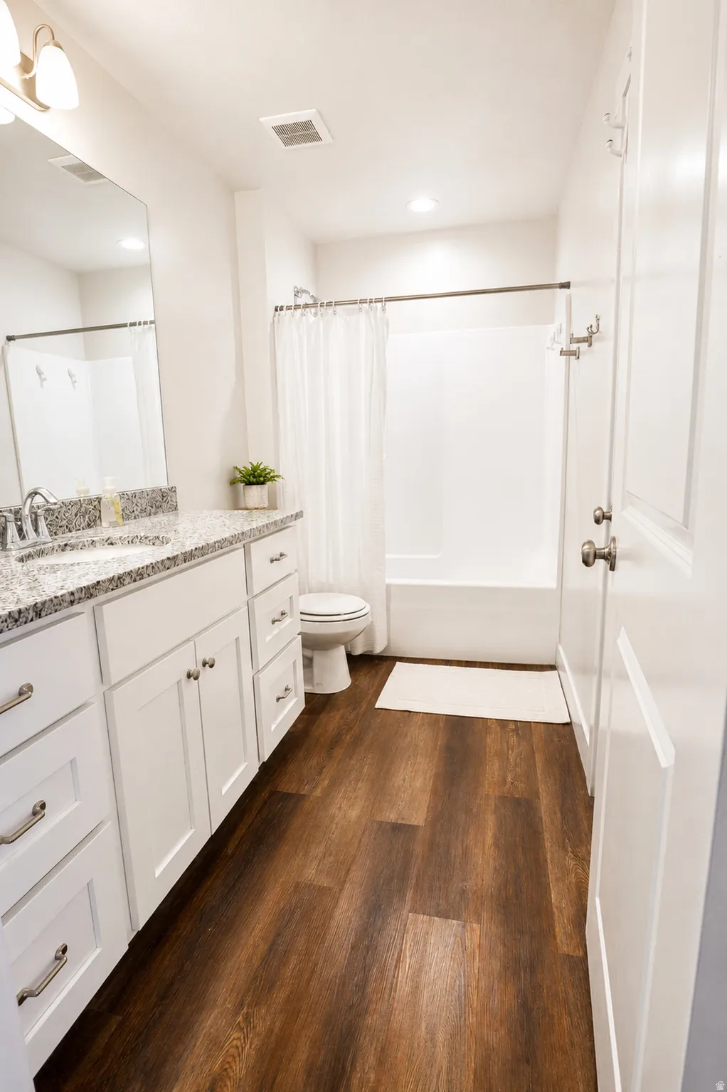 Bathroom featuring a white vanity with shaker-style cabinetry, a speckled countertop, and wood-finish flooring