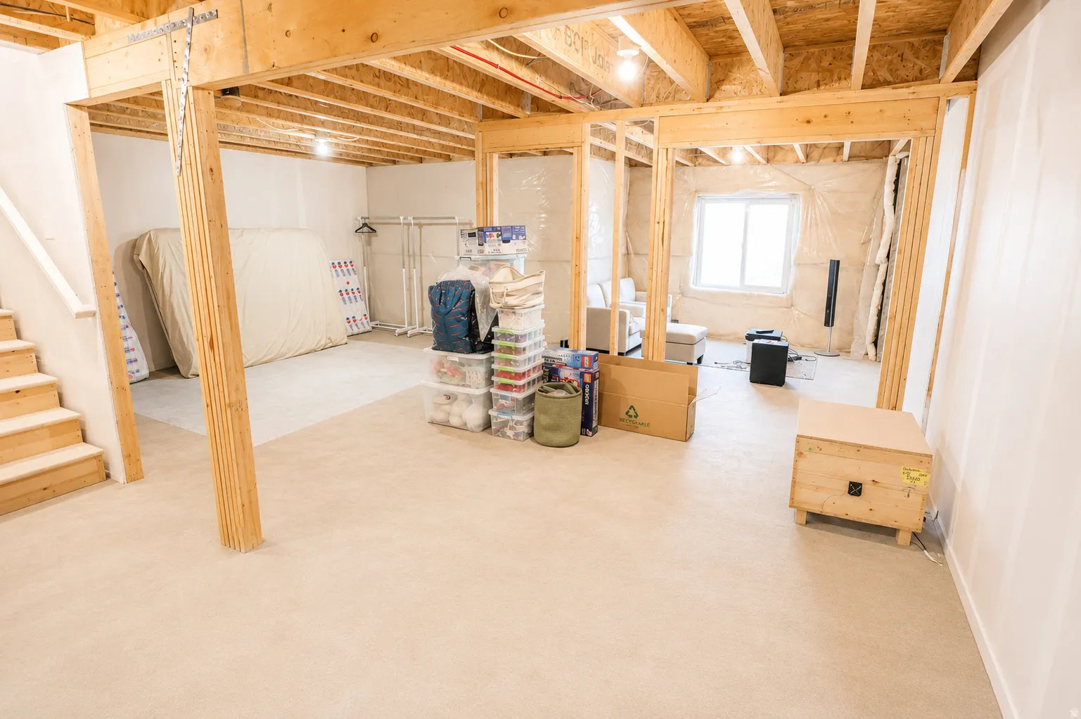 Unfinished lower level featuring exposed wood framing, wood stairs, and a window providing natural light