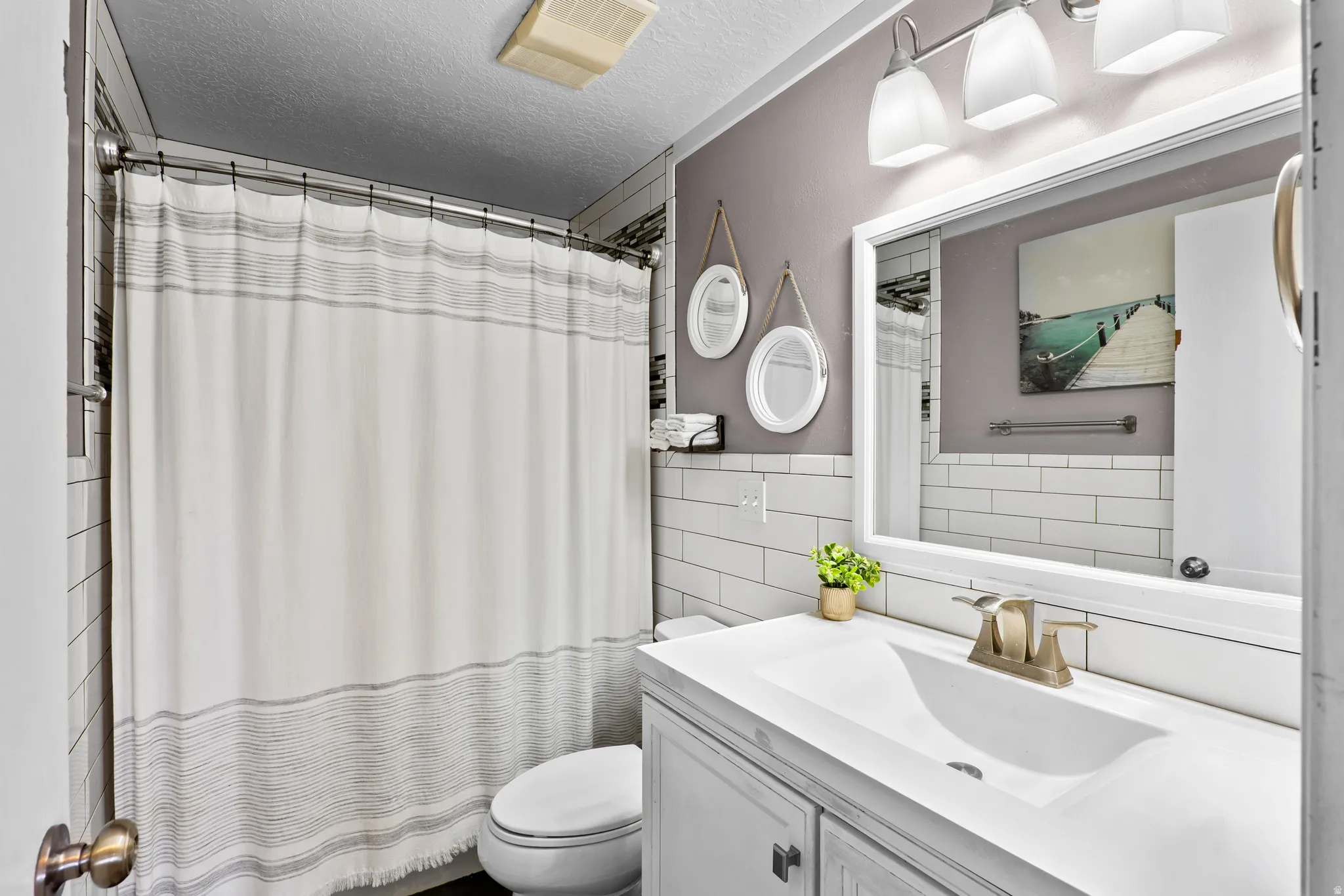 Bathroom featuring a white vanity with integrated sink, brushed nickel faucet, wall-mounted mirror, and three-light vanity fixture