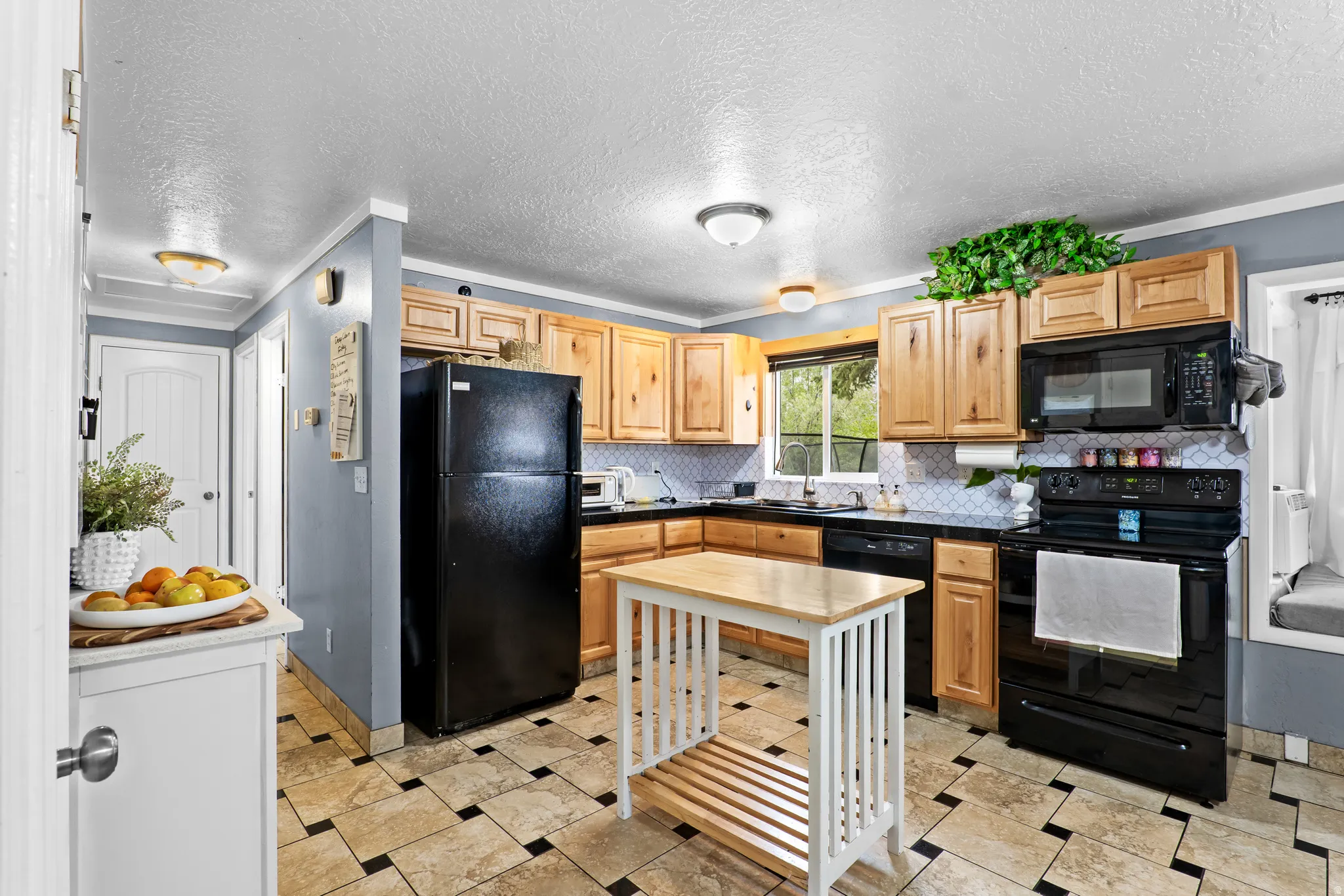 Kitchen featuring wood cabinetry, black appliances, dark countertops, and a white geometric tile backsplash