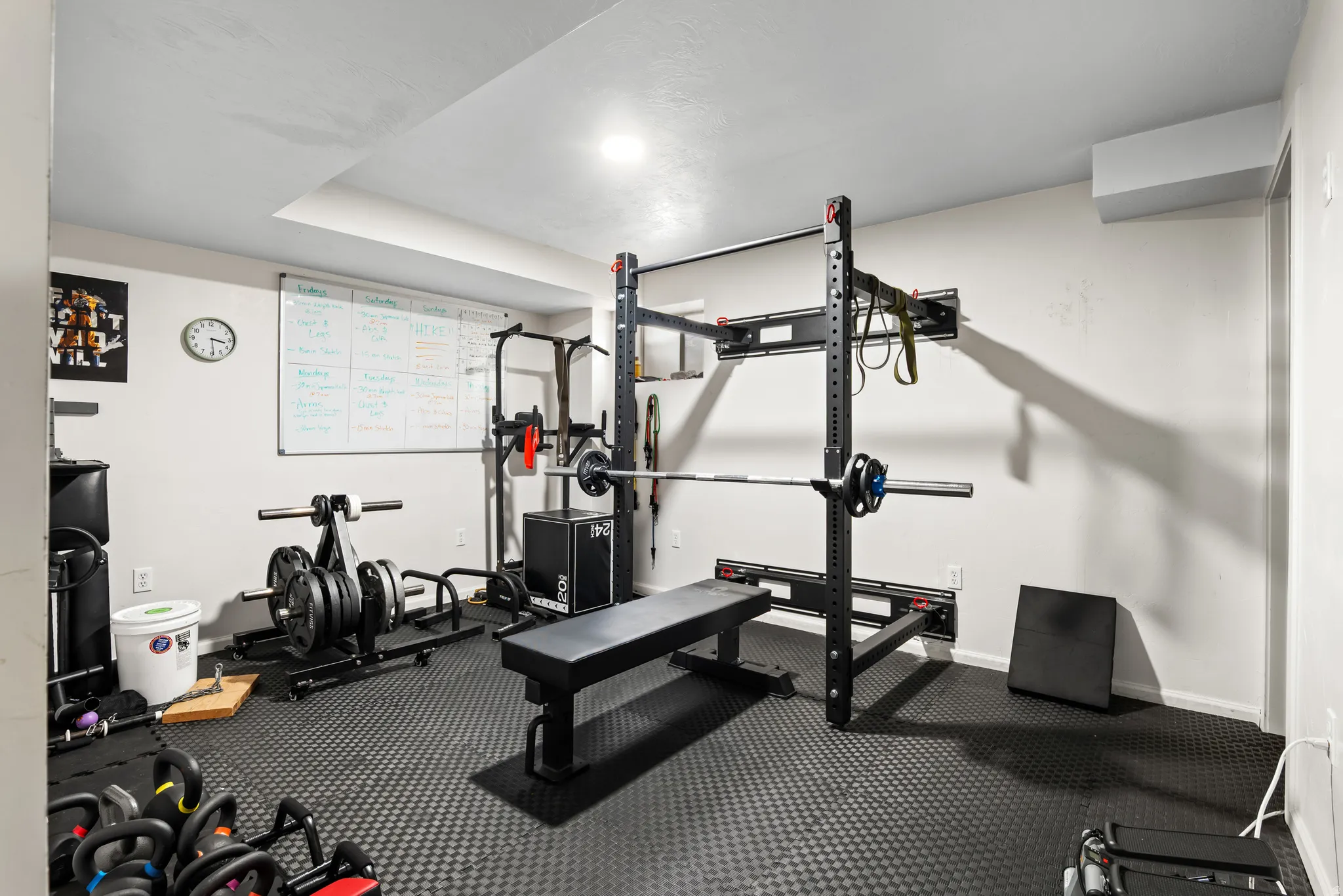 Dedicated fitness space featuring textured rubber flooring, white walls, recessed ceiling lighting, and a wall-mounted whiteboard