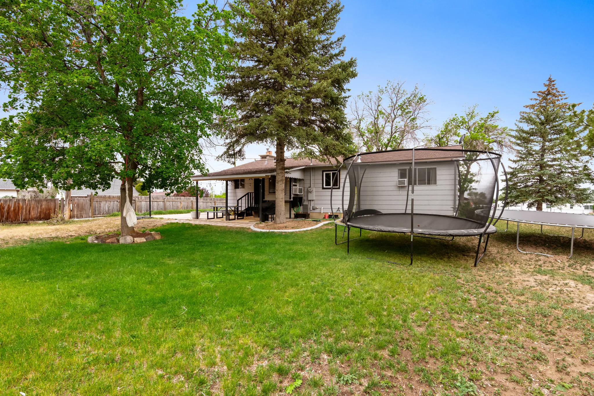 Spacious backyard featuring a covered patio, mature trees, manicured lawn, and wood privacy fencing