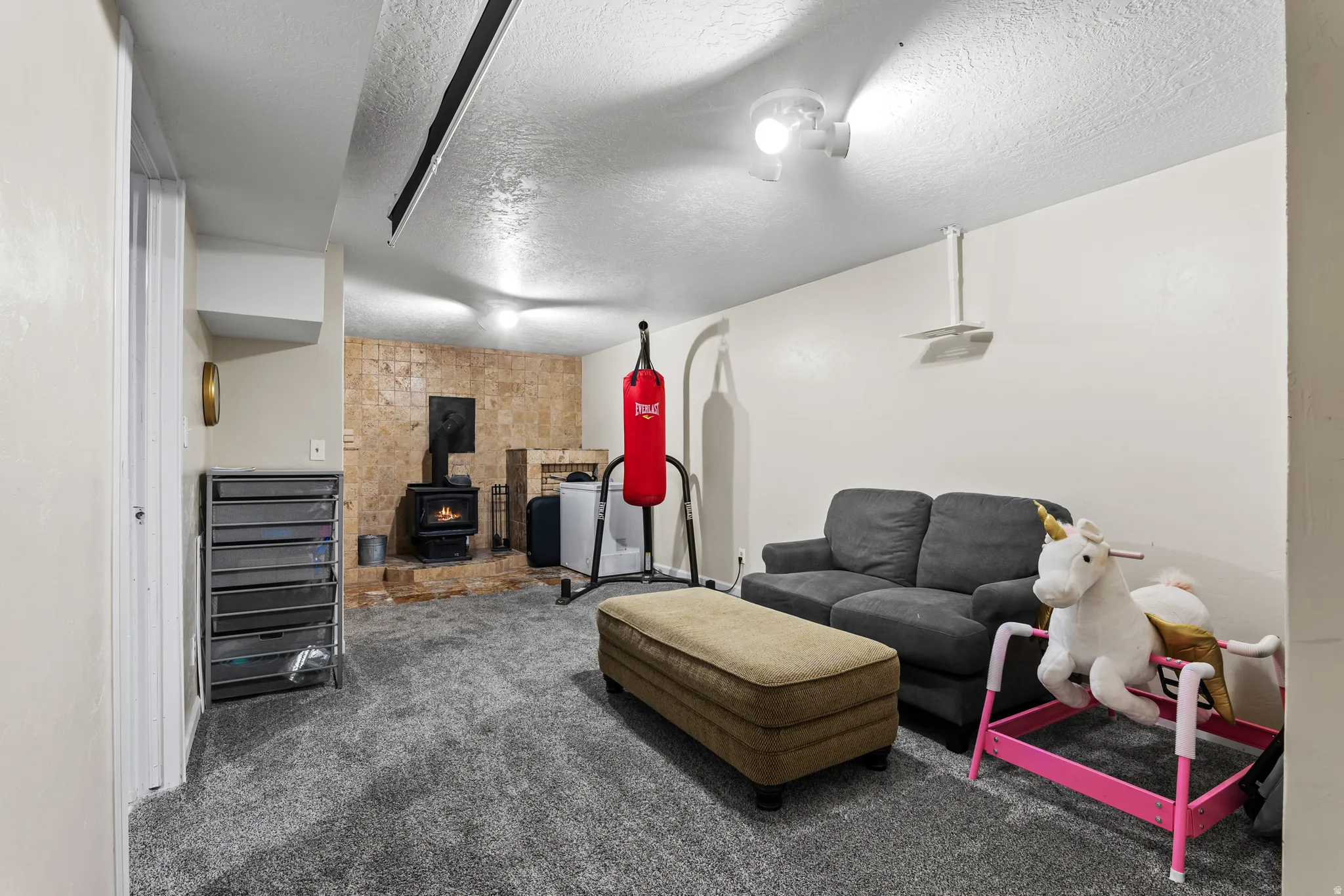 Carpeted recreation room featuring a corner fireplace with a stone-finish surround, light-colored walls, and ceiling-mounted lighting fixtures