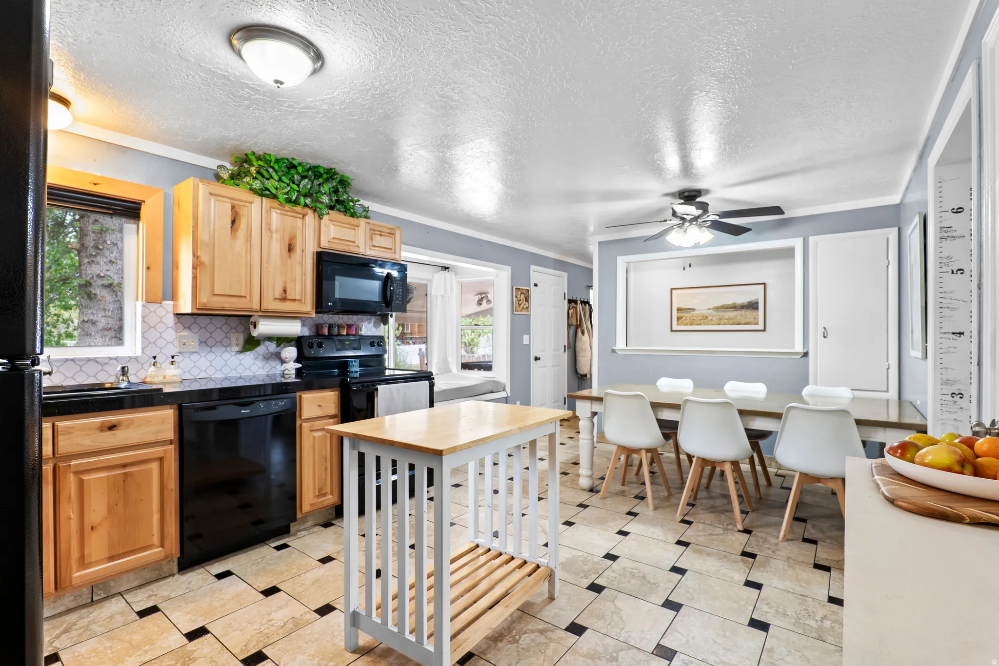 Kitchen and dining area featuring light wood cabinetry, black appliances, a patterned tile backsplash, and a light wood and white kitchen island
