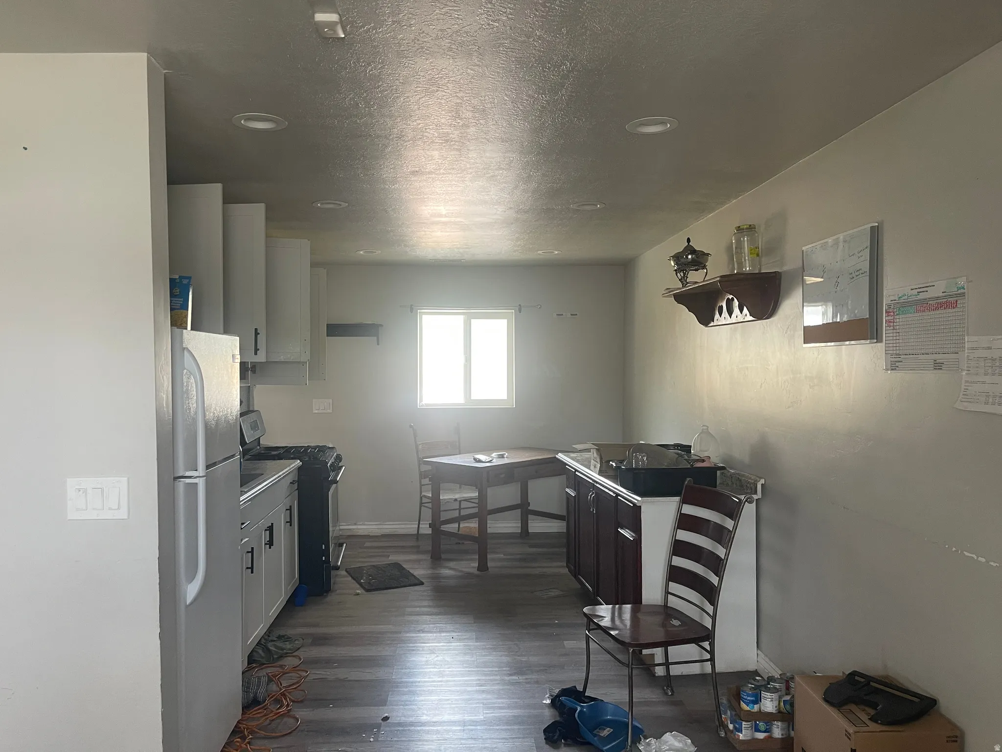 Kitchen featuring recessed ceiling lights, wood-finish flooring, white cabinetry, a window, and a stainless steel refrigerator