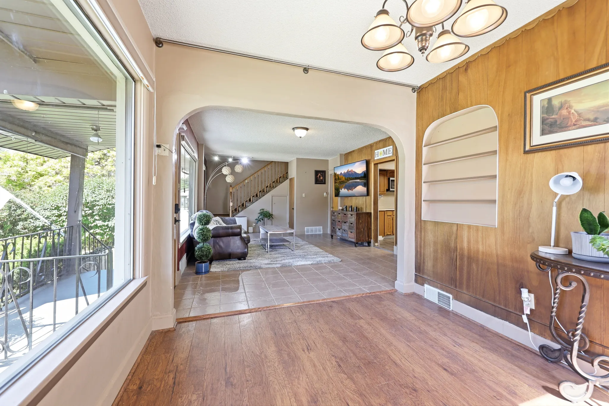 Open concept interior featuring distinct wood-finish flooring and tile flooring, an arched doorway, and a prominent wood panel accent wall with an integrated niche