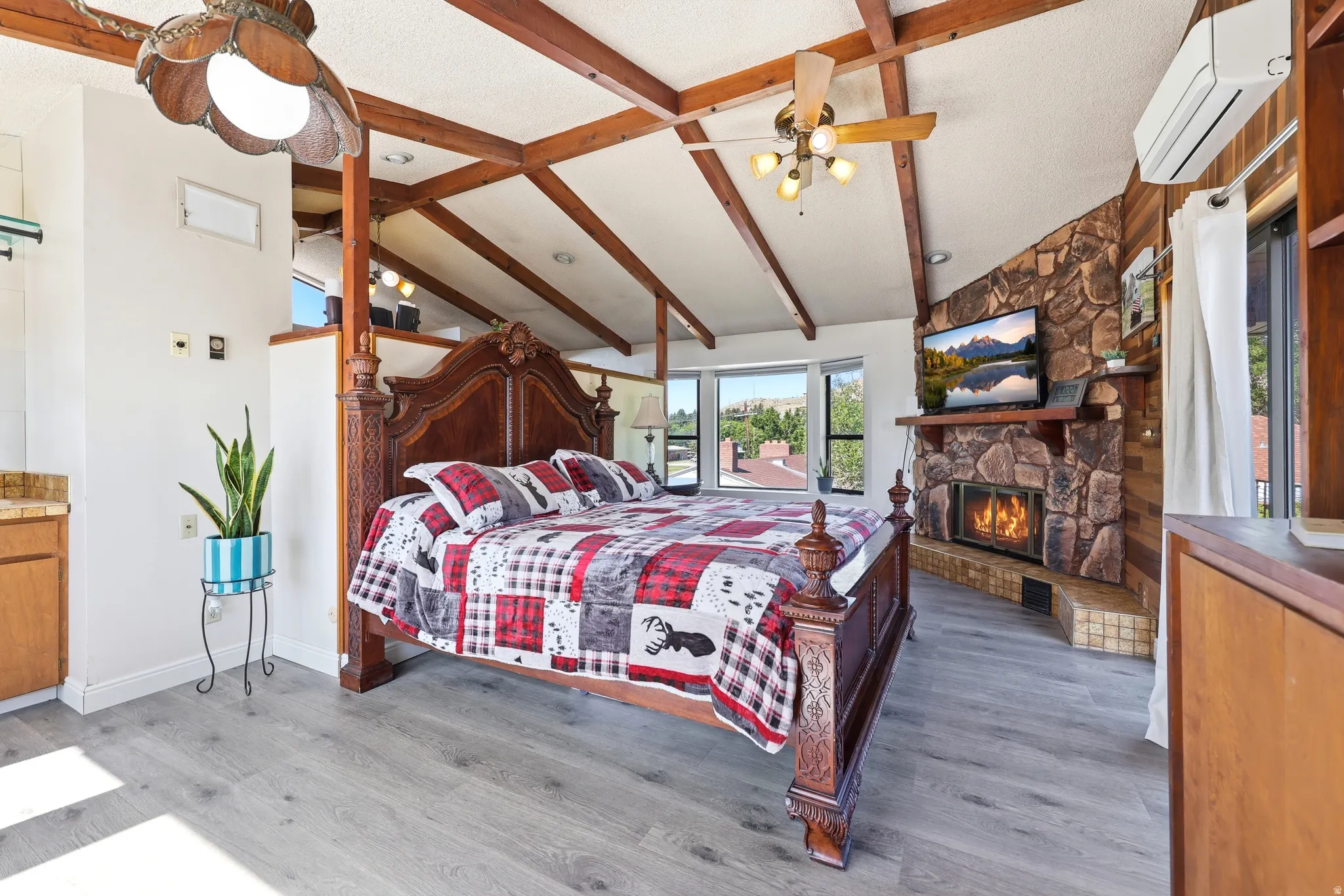 Spacious room featuring vaulted ceilings with exposed wood beams, a stone-faced fireplace with a tiled hearth, and light wood-finish flooring