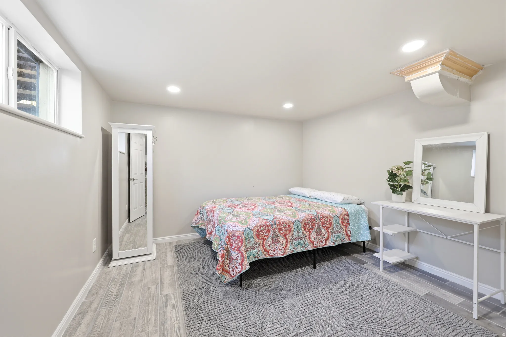Recessed lighting illuminates this room featuring wood-finish flooring, a window, and a white ceiling with a decorative wood accent