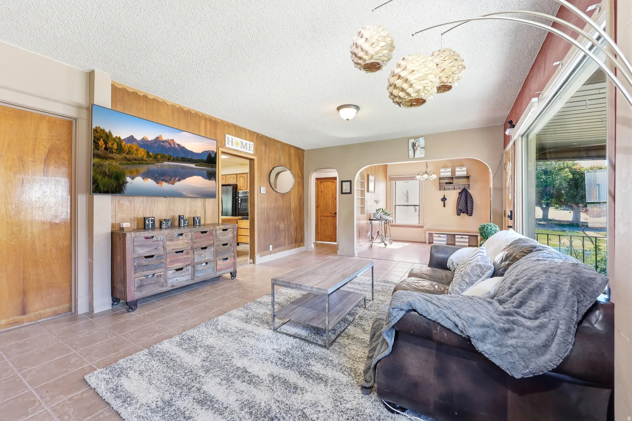 Living room featuring light-colored tile flooring, wood-paneled accent wall, and arched doorways