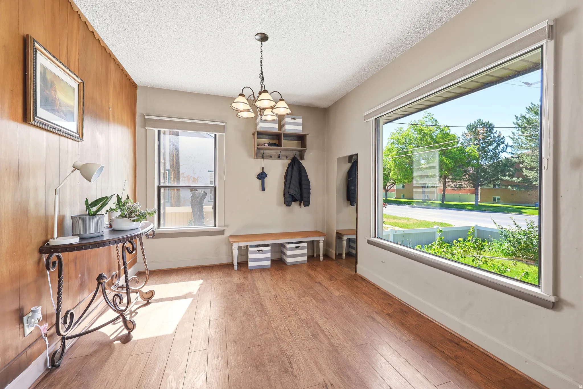 Spacious interior room featuring a large picture window, wood-finish flooring, and a paneled accent wall